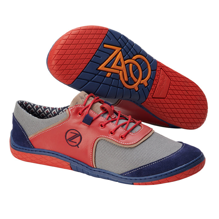 Schauen Sie sich die QOLE Red an, ein stylisches Paar Schuhe aus der Sneakerkollektion von ZAQQ. Sie haben leuchtend rote und blaue Gummisohlen mit einem geometrischen Muster und einem orangefarbenen Markennamen darunter. Der obere Teil ist grau mit auffälligen roten Akzenten, blauen Zehenkappen und wird durch kräftige rote Schnürsenkel und ein seitliches Logo abgerundet.