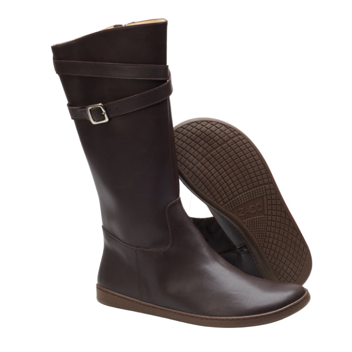 Ein Paar ATTRAQT Vegan Brown-Stiefel von ZAQQ in Dunkelbraun mit Schnallen und flachen, flexiblen Sohlen. Ein Stiefel steht aufrecht und zeigt sein Seitenprofil, während der andere auf der Seite liegt und die aufwendig gemusterte Sohle zeigt, die seine Barfußschuh-Eigenschaften hervorhebt.