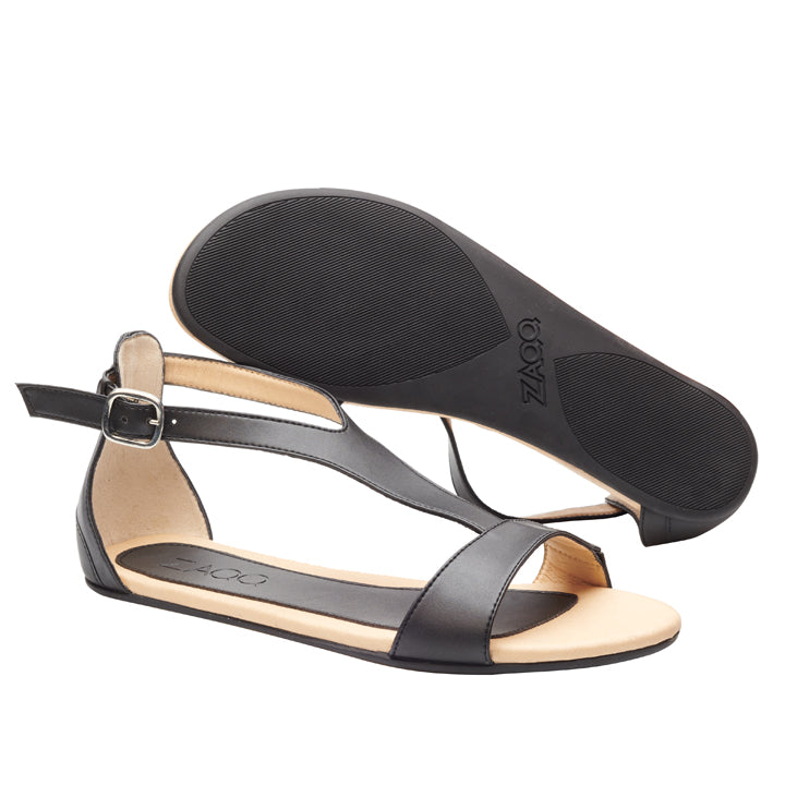 Die CLIQ Vegan Black Sandalen aus atmungsaktiven veganen Materialien haben offene Zehenpartien und Knöchelriemen. Eine Sandale hat eine silberne Schnalle an der Seite, während die andere ihre strukturierte Sohle hervorhebt. Der Markenname ZAQQ ist elegant in die Sohle dieser modischen veganen Barfußsandalen geprägt.