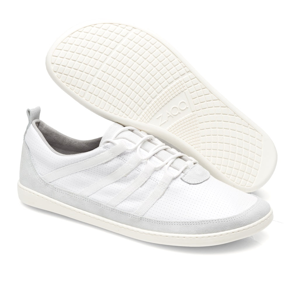 Ein Paar SPARQ Low White Sneaker von ZAQQ wird vor einem weißen Hintergrund präsentiert. Ein Schuh steht aufrecht und zeigt seine Seiten- und Draufsicht, während der andere angewinkelt ist, um die strukturierte Sohle hervorzuheben. Diese Sneaker zeichnen sich durch ein minimalistisches Design mit dezenten Nähten aus und sorgen für hervorragenden Komfort im Alltag.