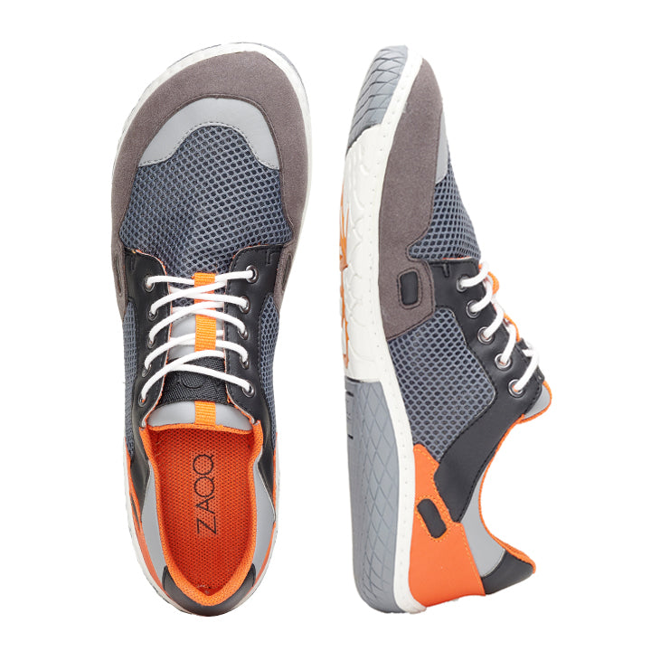 Wir präsentieren die NUQA Grey-Sneaker von ZAQQ: ein Sneaker von oben und der andere von der Seite, die ihr modernes Design zur Schau stellen. Diese Sneaker zeichnen sich durch eine Kombination aus grauem veganem Mesh-Gewebe mit leuchtend orangefarbenen Akzenten und weißen Sohlen aus, die mit der flexiblen ZAQQ MINIMAL-Technologie ausgestattet sind. Sie sind mit strahlend weißen Schnürsenkeln und schwarzen Details versehen und zeigen das ZAQQ-Branding deutlich im Schuhinneren.