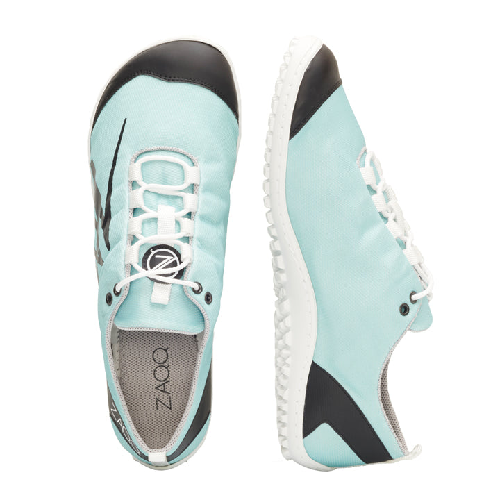 Die SQIM Turquoise Sneaker von ZAQQ sind aus veganem Recyclingstoff gefertigt und weisen einen hellblauen Farbton mit schwarzen Akzenten und weißen Sohlen auf. Diese Sneaker mit elastischen Schnürsenkeln zeichnen sich durch ein elegantes Design aus, wobei ein Schuh von oben und der andere von der Seite gezeigt wird.