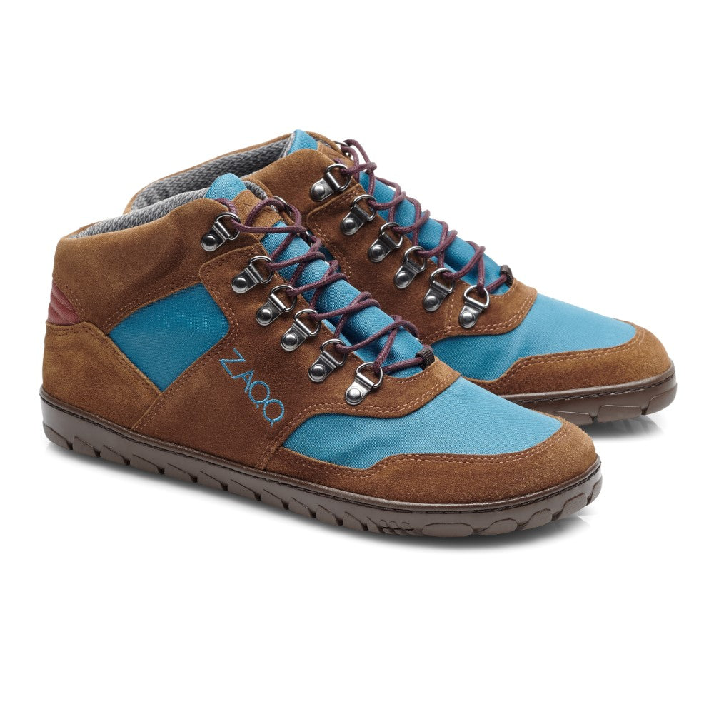 Diese HIQE Mid Blue Marine Waterproof Sneaker von ZAQQ sind ein stilvolles Paar High-Tops mit Akzenten aus braunem Wildleder, blauen Stoffeinsätzen und roten Details. Inspiriert vom Barfußschuh-Design verfügen diese Kicks über Metallösen, mehrfarbige Schnürsenkel und eine strukturierte braune Sohle. Das Markenlogo ist für ein elegantes Finish seitlich eingeprägt.