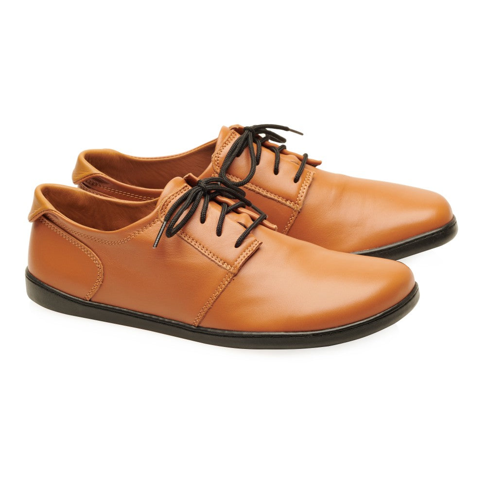 Ein Paar PIQUANT Nappa Cognac Lederschuhe von ZAQQ mit schwarzen Schnürsenkeln und Sohlen. Das elegante Design ist minimalistisch und geradlinig und zeigt ein niedriges Profil mit glatter Oberfläche. Die Schuhe aus Nappaleder stehen nebeneinander und sind leicht nach rechts geneigt.