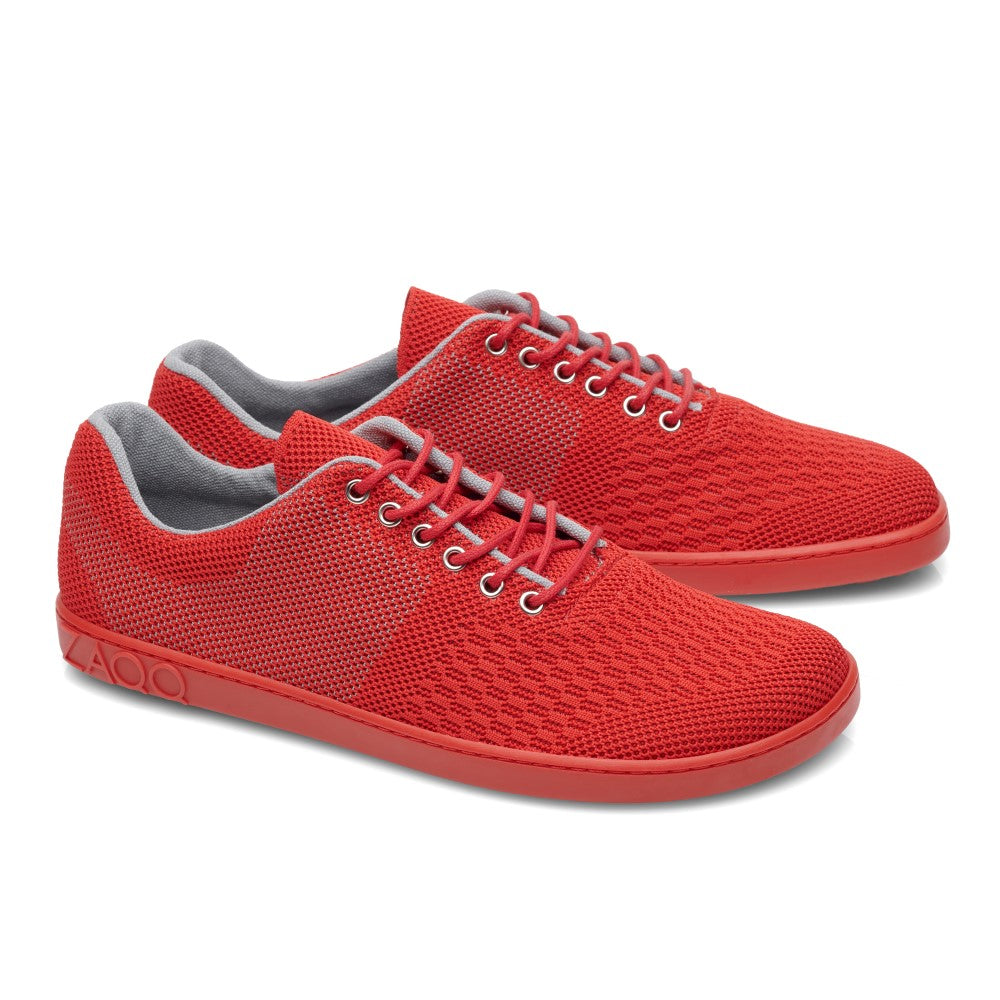 Nebeneinander werden die QNIT Red-Sneaker von ZAQQ gezeigt, die ein leuchtend rotes, veganfreundliches Mesh-Design, ein graues Innenfutter und weiße Schnürsenkel aufweisen. Diese Schuhe haben eine flache Sohle mit einem geprägten Logo an der Ferse.