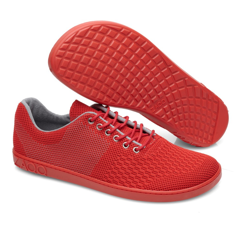 Die QNIT Red Sneaker von ZAQQ sind leuchtend rote, veganfreundliche Schuhe mit Mesh-Obermaterial und Gummisohle. Ein Schuh steht aufrecht, während der andere das Waffelmuster auf dem Profil zeigt. Sie verfügen über graue Innenteile und rote Schnürsenkel, die ihr stilvolles Strickgewebe-Design betonen.