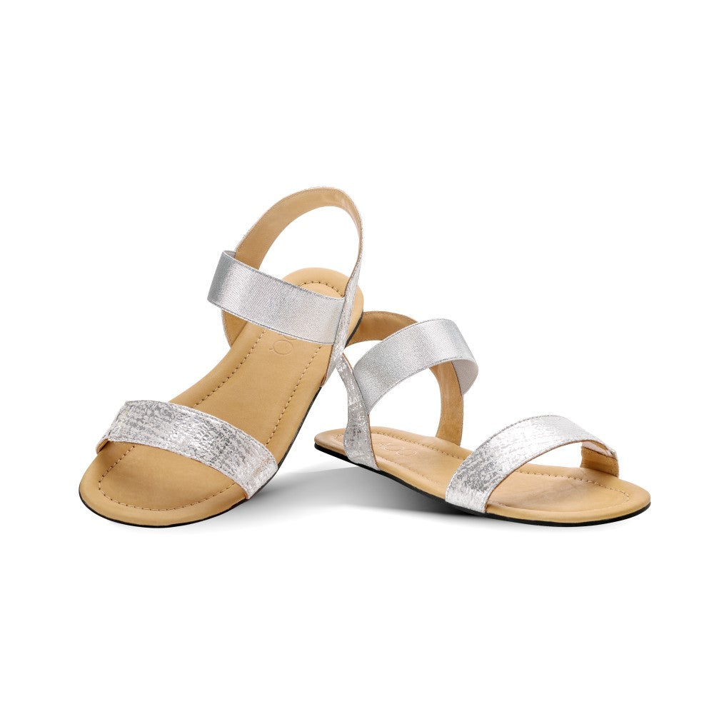 Die ZAQQ SLIQ-Silver Sandalen bestechen durch ihr minimalistisches Design mit eleganten Doppelriemen über dem Fuß und einem eleganten Knöchelriemen. Sie sind aus Nappaleder gefertigt und verfügen über eine schwarze Sohle gepaart mit hellbraunen Innensohlen, alles vor einem schlichten weißen Hintergrund.