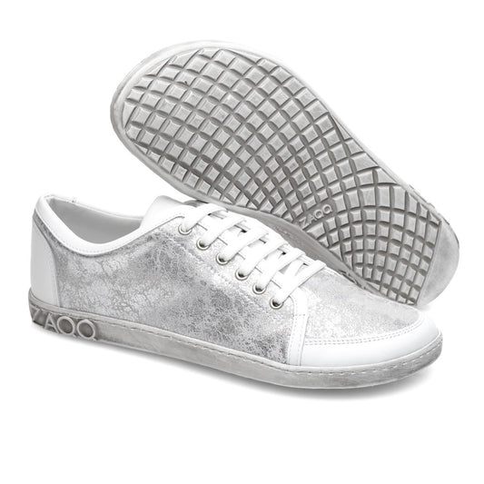 Die TIQQ Silver White Sneaker von ZAQQ zeichnen sich durch ein stilvolles Design mit einem strukturierten grauen Muster auf der weißen Oberfläche aus. Ein Sneaker steht aufrecht und zeigt die sichtbaren Schnürsenkel, während der andere die markante Sohle mit Waffelmuster zeigt. Sie sind aus hochwertigem Nappaleder gefertigt und zeigen stolz das ZAQQ-Logo an der Seite der Sohle.